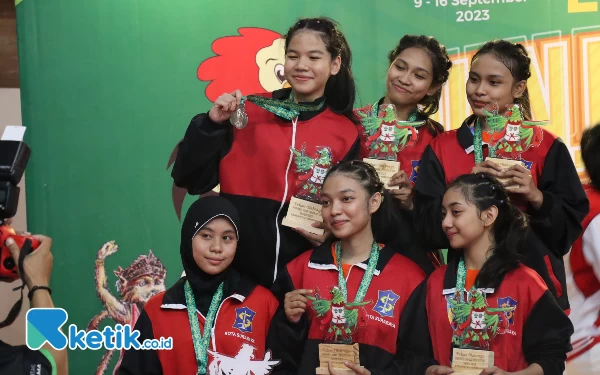 Thumbnail Senyum merekah dari tim kempo beregu putri Kota Surabaya juga tak kalah ceria merayakan medali perak yang mereka raih di atas podium. (Foto: Rifat/Ketik.co.id)