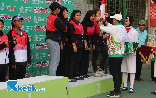 Thumbnail Ketua Pelti Jombang Mujtahidur Ridho mengalungkan medali perunggu kepada tim beregu putri Kota Surabaya. (Foto: Rifat/Ketik.co.id)